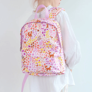 A child wearing the backpack, shown from the side against a neutral wall. You can see the bag’s main compartment and the floral‑fox print. The child’s white outfit highlights the pastel color palette of the design.
