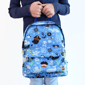 A child stands, holding the pirate‑design backpack by its top handle. The front pocket appear functional, and the playful print stands out against the kid’s outfit.